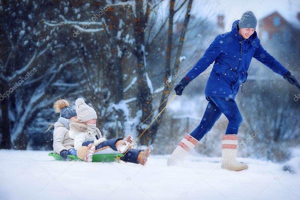 Little girls enjoying sledding. Father sledding his little adorable daughters. Family vacation on Christmas eve outdoors