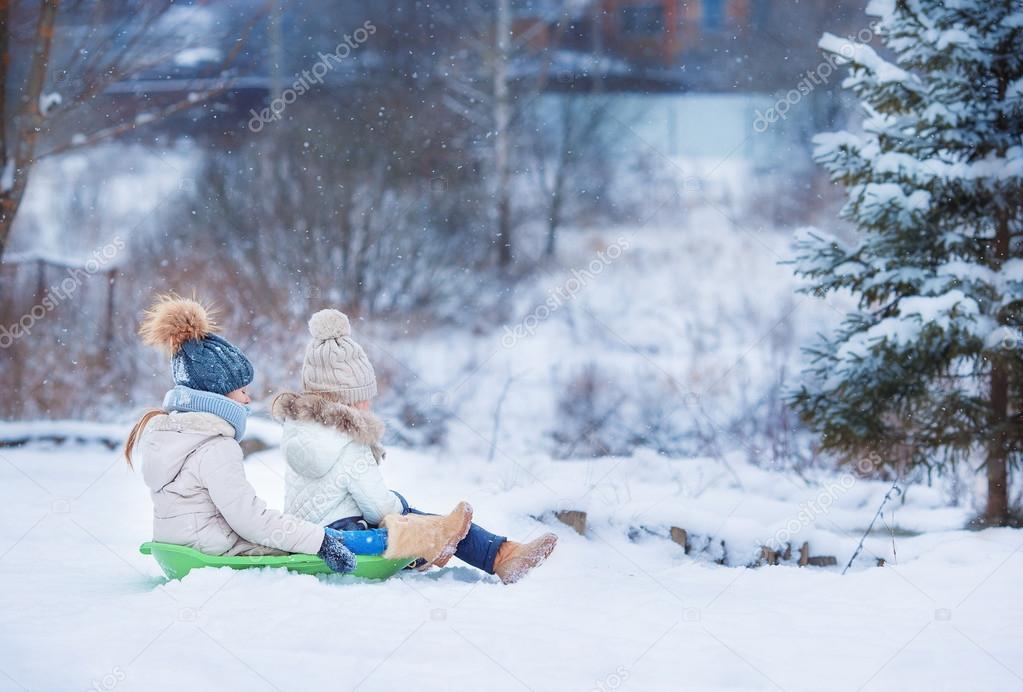 Little adorable girls enjoy a sleigh ride. Child sledding. Children play outdoors in snow. Family vacation on Christmas eve outdoors