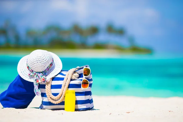 Blue bag, straw white hat, sunglasses and sunscreen bottle on tropical beach — Stock Photo, Image