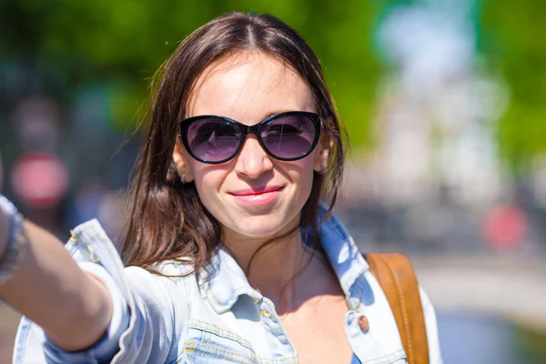 Mladá žena s autoportrét v Evropské město venku. Mladý dospělý drží smartphone fotoaparát vyfotit sebe během své letní dovolené v Amsterdamu — Stock fotografie