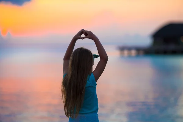 Silhouet van meisje maken van hart bij zonsondergang op het strand — Stockfoto