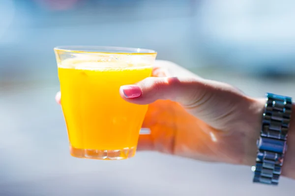 Hand holding glass with fresh orange juice in outdoor cafe — Stock Photo, Image