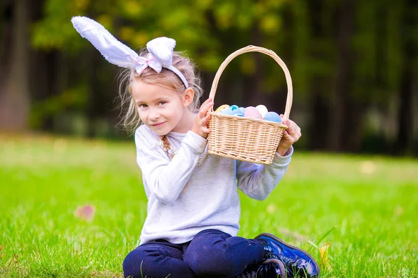 Adorable little girl wearing bunny ears holding a basket with Easter eggs on spring day — Stock Photo, Image