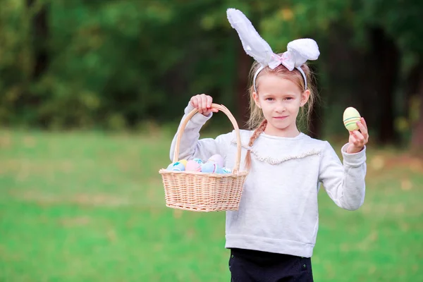 Entzückendes kleines Mädchen mit Hasenohren, das am Frühlingstag einen Korb mit Ostereiern hält — Stockfoto