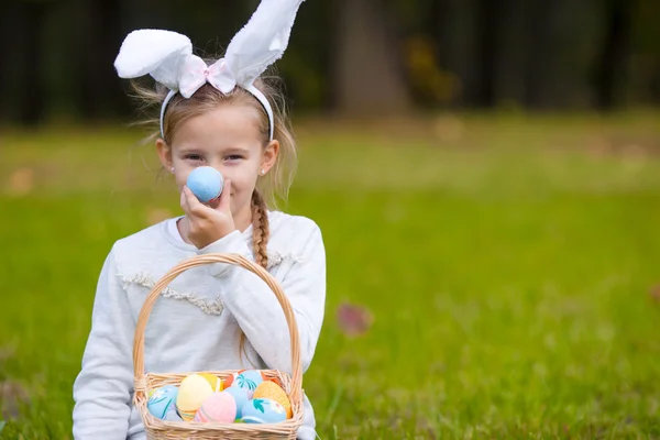 Adorable little girl wearing bunny ears playing with Easter eggs on spring day outdoors — Stock Photo, Image