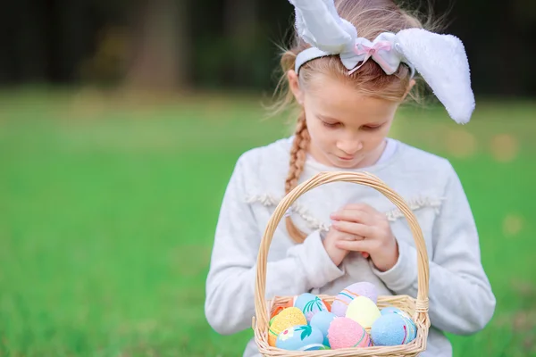 Carina bambina con le orecchie da coniglio in possesso di un cesto con uova di Pasqua il giorno di primavera — Foto Stock