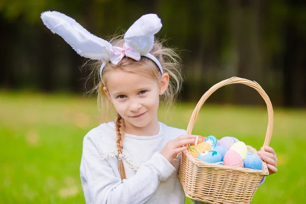 Entzückendes kleines Mädchen trägt Hasenohren mit einem Korb voller Ostereier an einem Frühlingstag im Freien — Stockfoto
