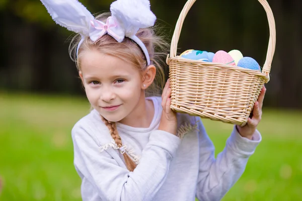 Portrait of little girl wearing bunny ears with a basket full Easter eggs on spring day outdoors — Stock Photo, Image