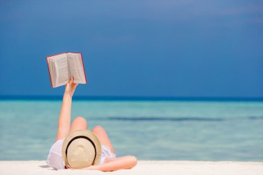 Genç kız tropikal beyaz kumsalda yalan bir kitap okuyor