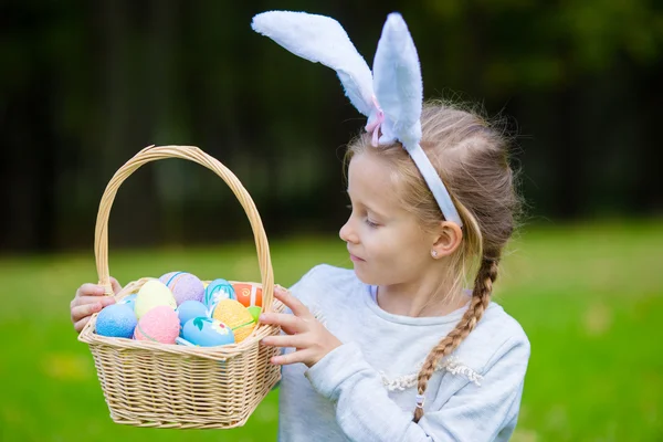 Adorable little girl wearing bunny ears holding a basket with Easter eggs on spring day — Stock Photo, Image