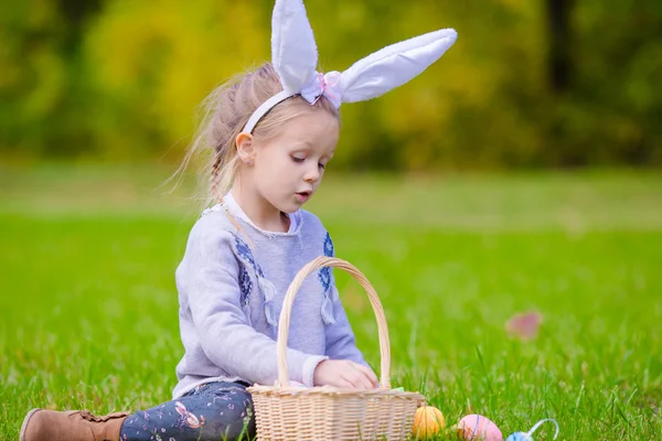 Carina bambina con le orecchie da coniglio che gioca con le uova di Pasqua il giorno di primavera all'aperto — Foto Stock