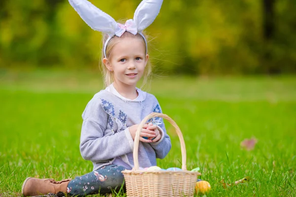 Adorabile bambina che indossa orecchie da coniglio con un cesto pieno di uova di Pasqua il giorno di primavera all'aperto — Foto Stock