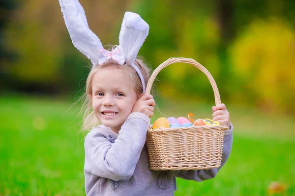 Fröhliches kleines Mädchen mit Hasenohren und einem Korb voller Ostereier an einem Frühlingstag im Freien — Stockfoto