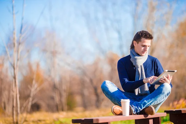 Hombre joven tomando café con teléfono en el parque de otoño al aire libre —  Fotos de Stock