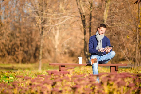 Hombre joven tomando café con teléfono en el parque de otoño al aire libre —  Fotos de Stock