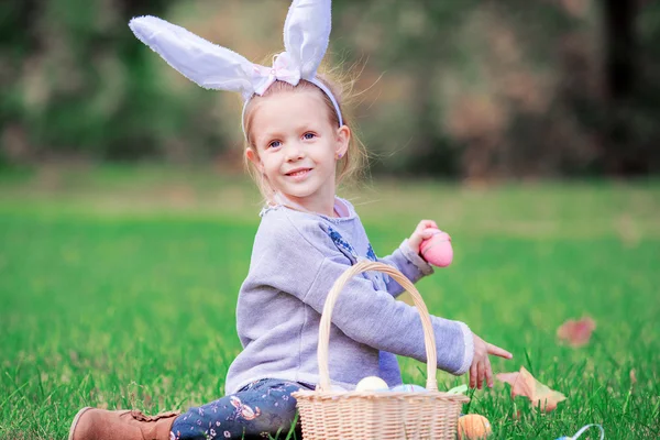 Entzückendes kleines Mädchen trägt Hasenohren mit einem Korb voller Ostereier an einem Frühlingstag im Freien — Stockfoto