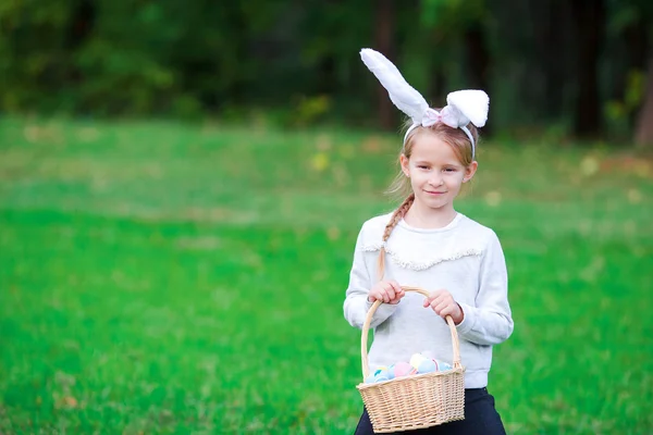 Entzückendes kleines Mädchen mit Hasenohren, das am Frühlingstag einen Korb mit Ostereiern hält — Stockfoto