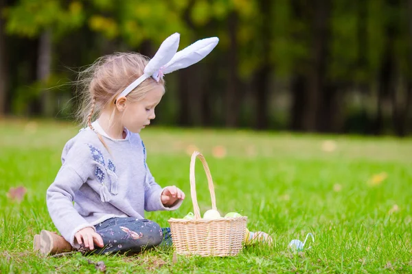 Adorable little girl wearing bunny ears playing with Easter eggs on spring day outdoors — Stock Photo, Image