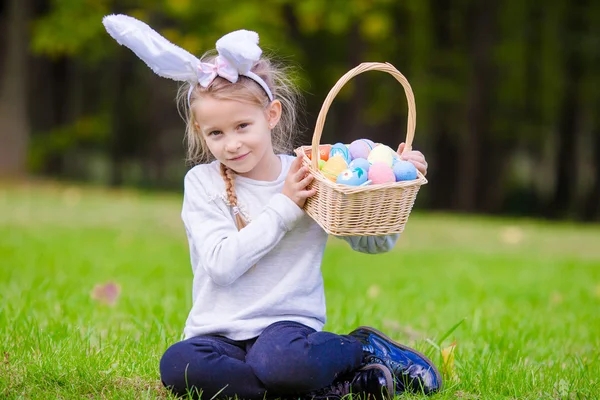 Attraktives kleines Mädchen mit Hasenohren und einem Korb voller Ostereier an einem Frühlingstag im Freien — Stockfoto