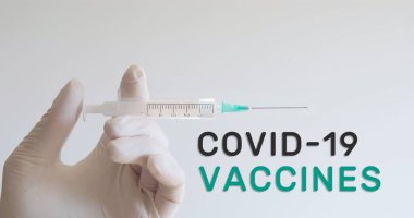 Eldivenli el şırıngayı Covid-19 aşı metninin yanında tutuyor. Coronavirus aşısı konsepti.
