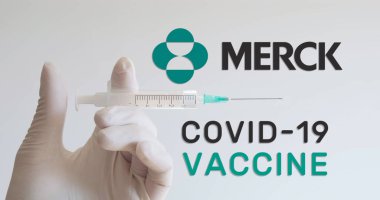 Eldivenli el, Coronavirus (Covid-19) aşısı geliştiren şirketlerden biri olan Merck logosunun yanında şırınga tutuyor. Viyana, Avusturya - 18 Ocak 2021