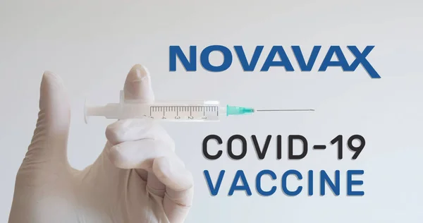 Eldivenli el, bir Covid-19 (Coronavirus) aşısı geliştiren şirketlerden biri olan Novavax logosunun yanında şırınga tutuyor. Viyana, Avusturya - 18 Ocak 2021