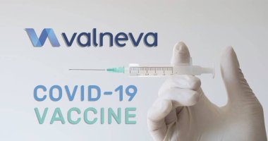 Eldivenli el, bir Covid-19 (Coronavirus) aşısı geliştiren şirketlerden biri olan Valneva logosunun yanında şırınga tutuyor. Viyana, Avusturya - 18 Ocak 2021