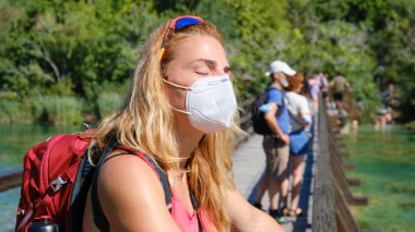 Sırt çantalı ve maskeli kadın turist Krka Ulusal Parkı 'nda dinleniyor. Turizm, Hırvatistan, Yaz.