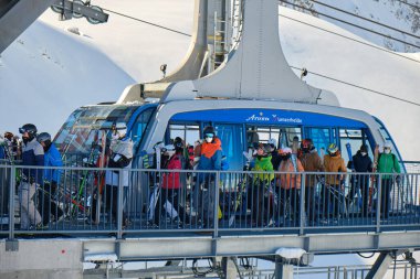 Tıbbi maskeli kayakçılar Urdenbahn teleferiğinden Arosa Lenzerheide kayak merkezindeki Kış mevsimi için Covid-19 düzenlemelerinin bir parçası olarak çıkıyorlar. İsviçre - 24 Mart 2021.