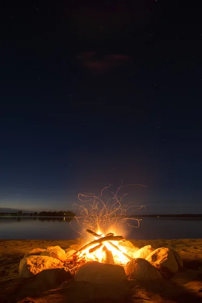 Fogo de acampamento de faísca ao lado do lago abaixo de um céu estrelado — Fotografia de Stock