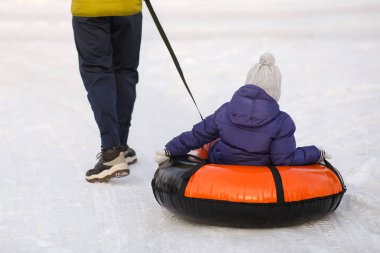 Babam tüpten şişme bir yüzük takan küçük bir kızı çekiyor. Kış, eğlence, açık hava oyunları. Yürüyüş sporları. Dikiz aynasından yakından bak. Kış kar arka planı.
