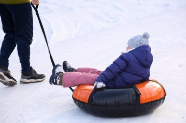 Babam tüpten şişme bir yüzük takan küçük bir kızı çekiyor. Kış, eğlence, açık hava oyunları. Yürüyüş sporları. Dikiz aynasından yakından bak. Kış kar arka planı.