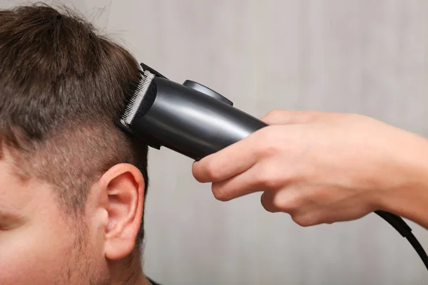 hair clipper in hand while cutting. Mens haircut. Dark hair salon.