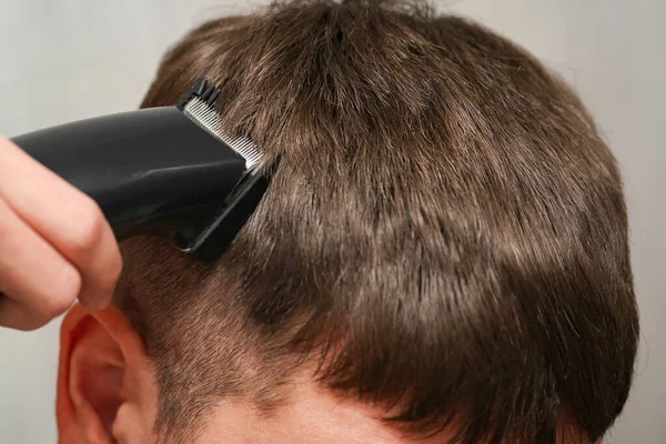 Tondeuse à cheveux à la main lors de la coupe. Une coupe de cheveux masculine. Salon de coiffure sombre. — Photo