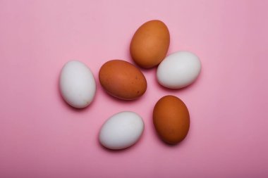 Pembe arka planda tavuk çiftliği beyaz ve kahverengi yumurtalar..
