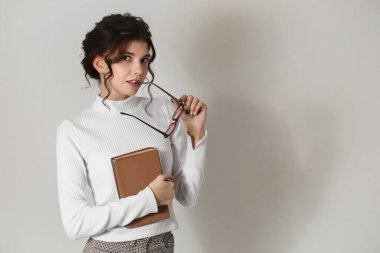 Ellerinde kitap ve gözlüklerle güzel, zeki bir genç kadın. Beyaz bir arka planda, katı bir iş kadını, öğretmen ya da öğrenci.