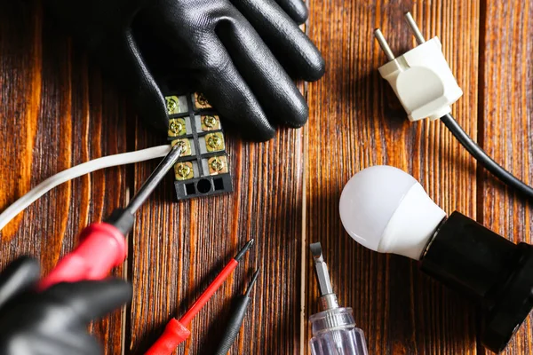 Un hombre que arregla una lámpara eléctrica, guantes dieléctricos, un destornillador. Conector de alambre, vista superior, fondo de madera. —  Fotos de Stock