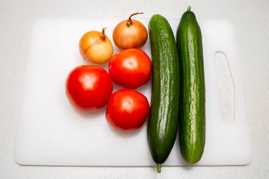 Onion heads, fresh tomatoes and cucumbers on cutting board
