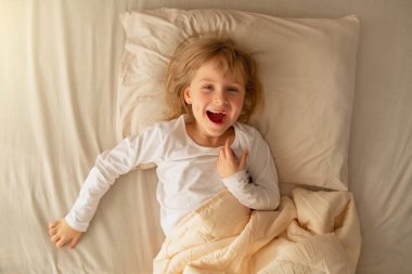 Sabahın erken saatlerinde, anaokulu kızı yatakta uzanıyor ve sağlıklı bir uykudan sonra eğleniyor. Egzersiz yapıyorum, günaydın..