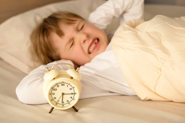 A girl, a female child, has covered his ears with his hands when the alarm clock rings loudly in the morning. Refusing to get up early in the morning.