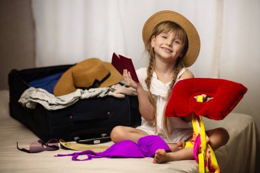 Seyahat konsepti. Çantası ve pasaportu olan mutlu kız çocuğu tatile, seyahate hazırlanıyor. Neşe ve mutluluk, yüzünde bir gülümseme.