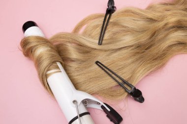 Pembe arka planda geniş çaplı saç maşasında kıvırcık sarı saç. Kıvırcık bakım, saç stili, siyah tokalar..