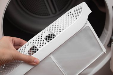 Bir kadın eli kurutma makinesinin filtresini çıkarır. Çamaşır kurutma makineleri için filtre indir. Makineyi kullandıktan sonra kurutucunun kirli hava filtresinden kabartılıyor.