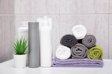 Farklı renkte pamuklu havlular, şampuan ve merhem şişeleri, banyoda saksıda bir bitki. Doğal kozmetik ve saç bakımı kavramı.
