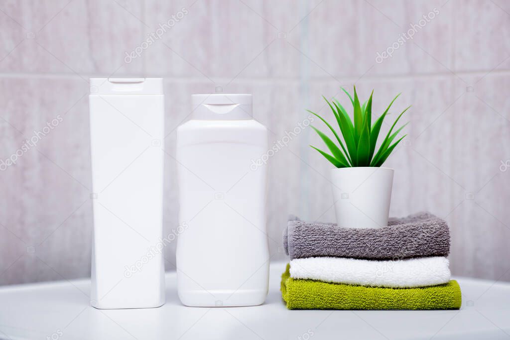 Rolled cotton fluffy towels of different colors, bottles of shampoos and balms, a plant in a pot in the bathroom. The concept of natural cosmetics and hair care.