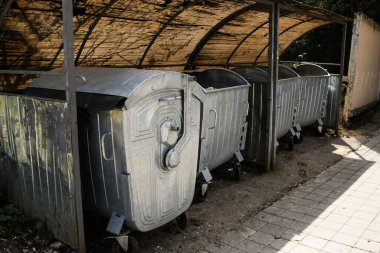 Güneşli bir caddede arka arkaya büyük gri çöp konteynırlarını boşalt. Sokaktaki gri metal çöp tenekeleri.