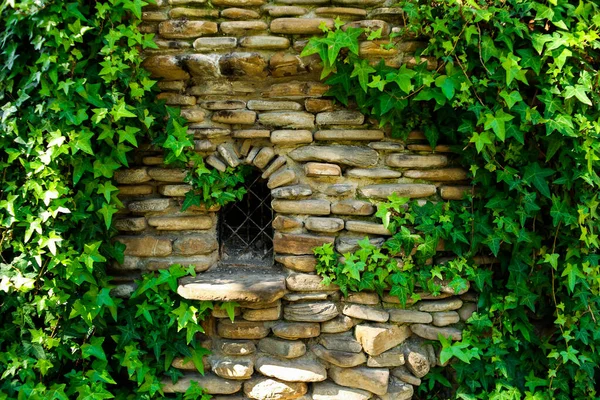 Una antigua ventana en una casa hecha de piedras, cubierta de hiedra. Casa de cuento de hadas. —  Fotos de Stock