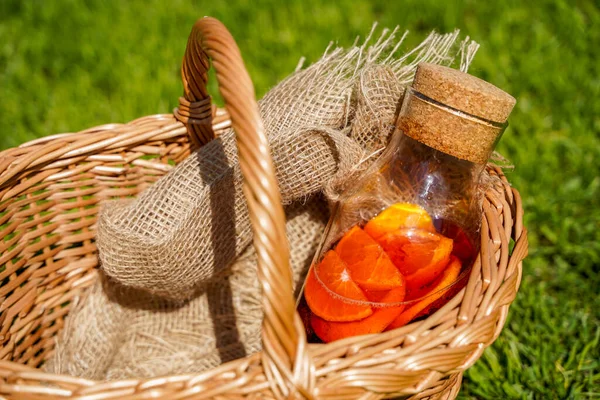 Une bouteille de soda naturel fait maison avec des baies et des oranges, des aliments biologiques purs et des boissons dans un style rustique. Oranges, jus et un panier sur l'herbe verte. — Photo