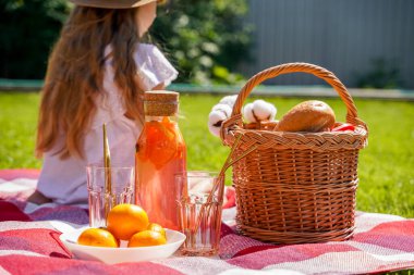 Çimlerin üzerinde piknik, kırmızı bir ekose battaniye, hasır bir sepet, portakal ve böğürtlenlerden yapılmış doğal bir içecek, bir somun ekmek. Yazın dışarıda nefis atıştırmalıklar.