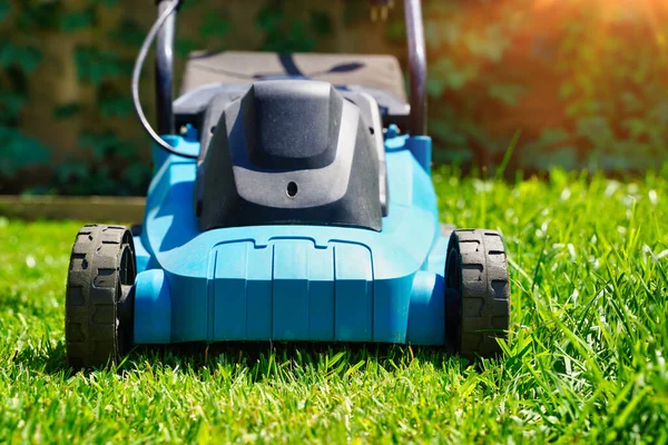 Cortacésped en un césped verde exuberante, la mitad de la hierba recortada. Patio trasero de la casa. — Foto de Stock